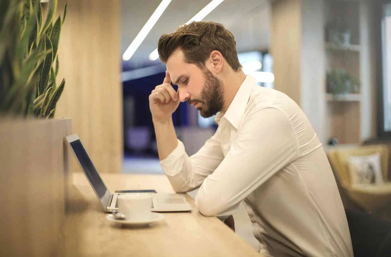 Mann sitzt mit Kopfschmerzen vor dem Laptop